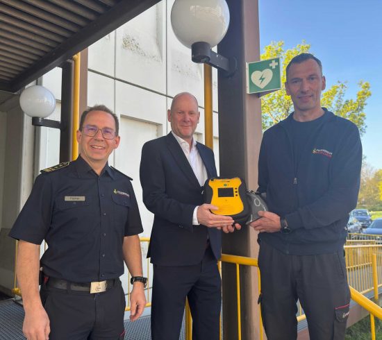Feuerwehrkommandant Sebastian Fischer, Erster Bürgermeister Dirk Büscher und Notfallsanitäter sowie Praxisanleiter Stephan Bürkle (von links) stellen den neuen, öffentlich zugänglichen AED an der Hauptfeuerwache vor.