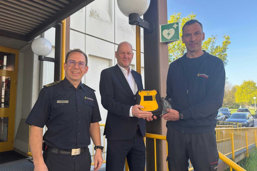 Feuerwehrkommandant Sebastian Fischer, Erster Bürgermeister Dirk Büscher und Notfallsanitäter sowie Praxisanleiter Stephan Bürkle (von links) stellen den neuen, öffentlich zugänglichen AED an der Hauptfeuerwache vor.