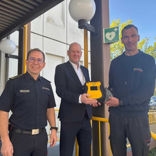 Feuerwehrkommandant Sebastian Fischer, Erster Bürgermeister Dirk Büscher und Notfallsanitäter sowie Praxisanleiter Stephan Bürkle (von links) stellen den neuen, öffentlich zugänglichen AED an der Hauptfeuerwache vor.